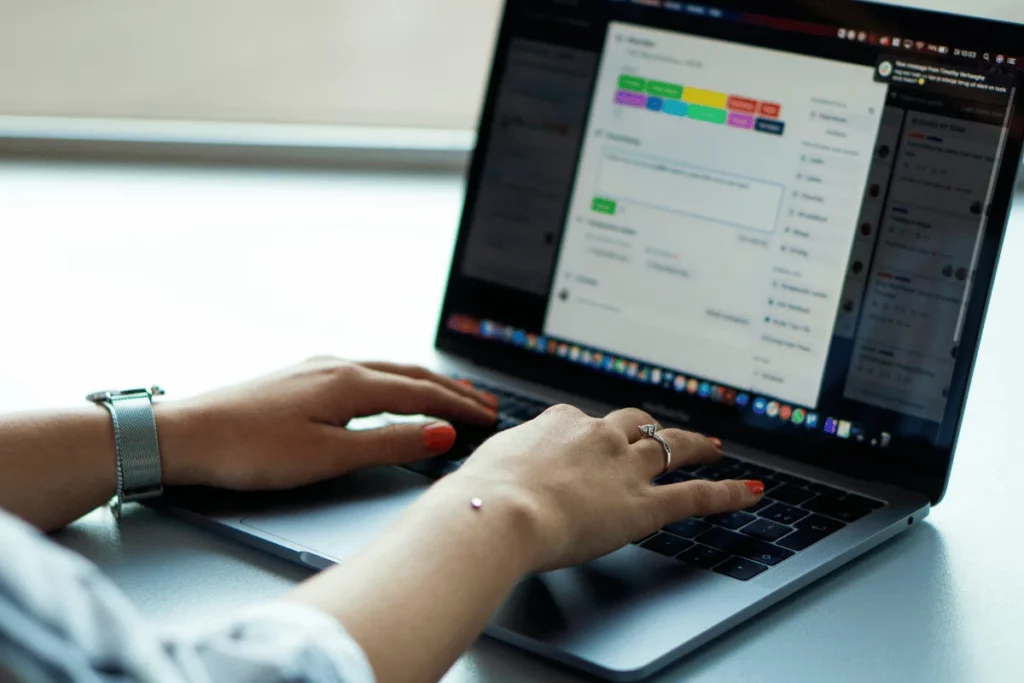 Close-up of hands typing on laptop with project management software.