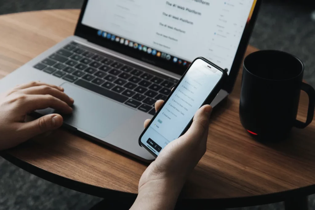 Person multitasking with laptop and smartphone at desk.