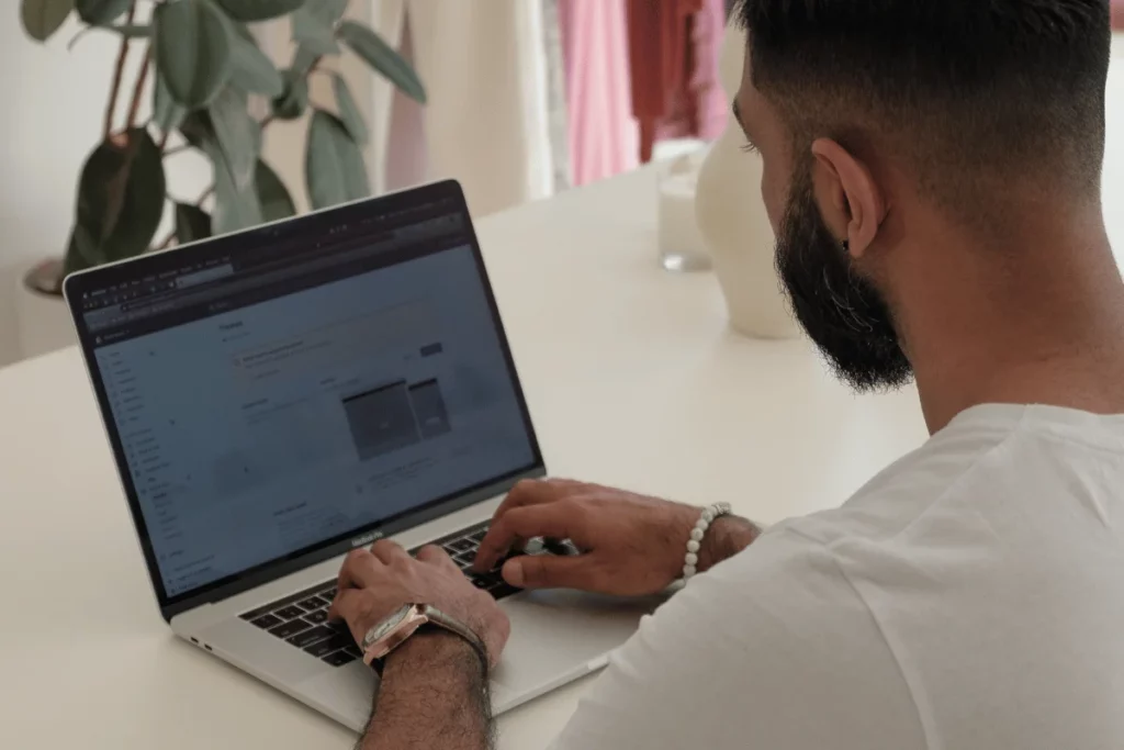 Man working on laptop at white desk with plant nearby.