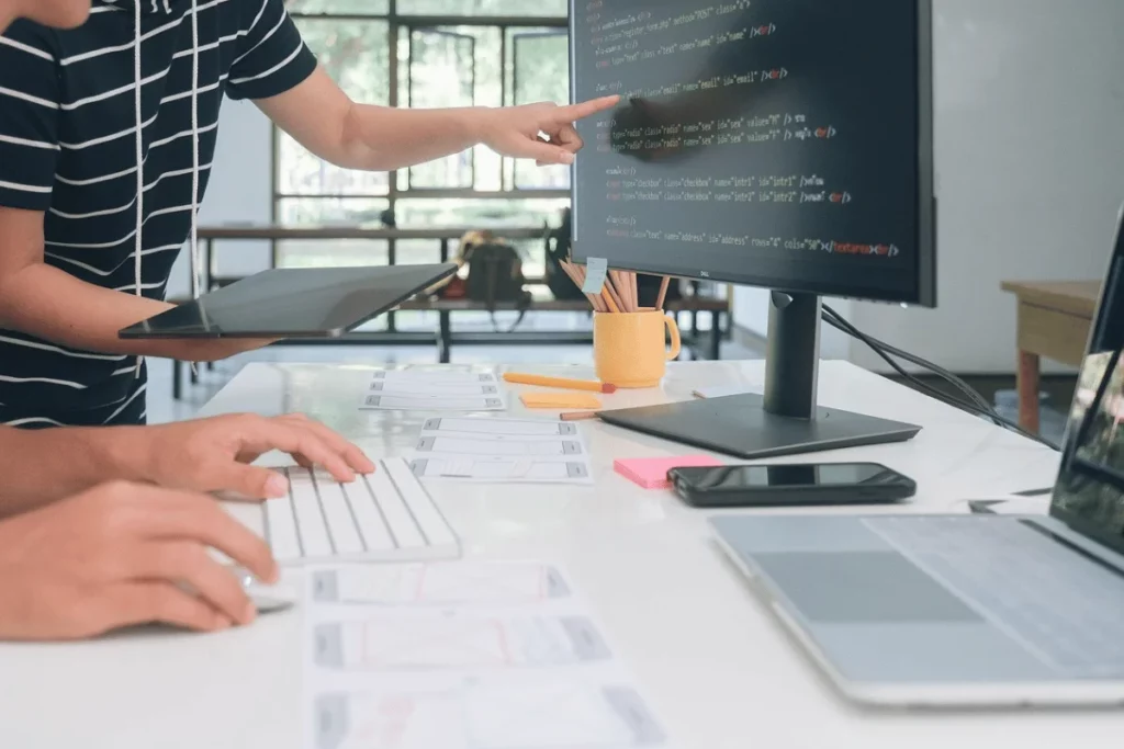 Programmer typing code while colleague points at computer screen.