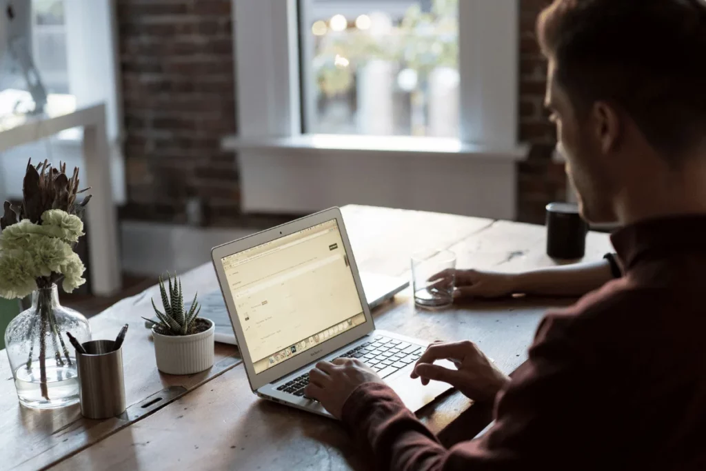 Person typing on MacBook with plants on desk.