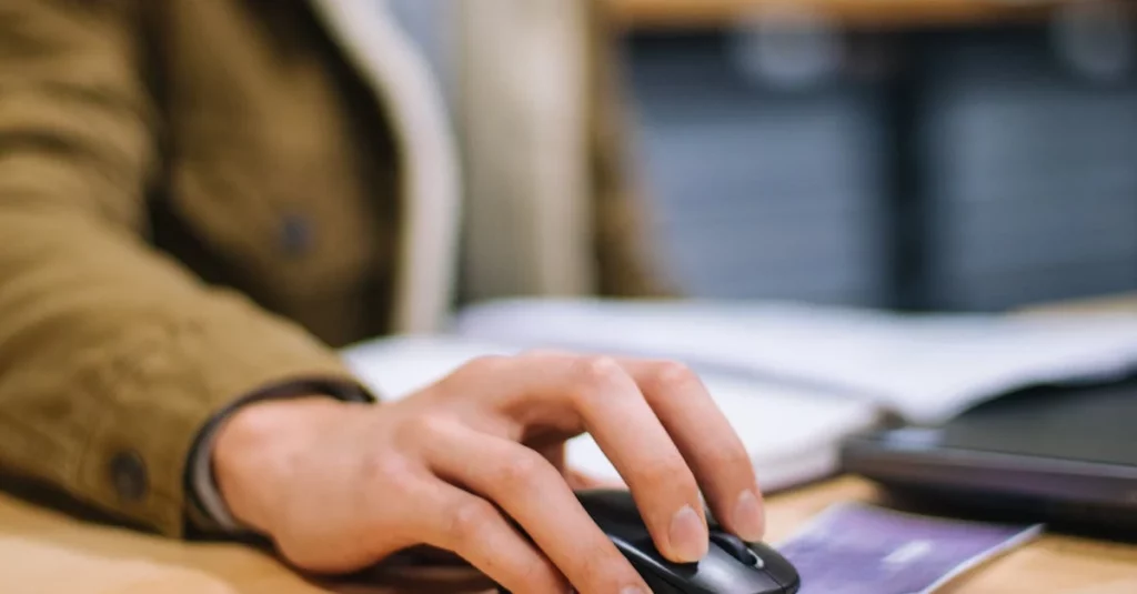 Person's hand using computer mouse at wooden desk with HTML widgets for conversion optimization.