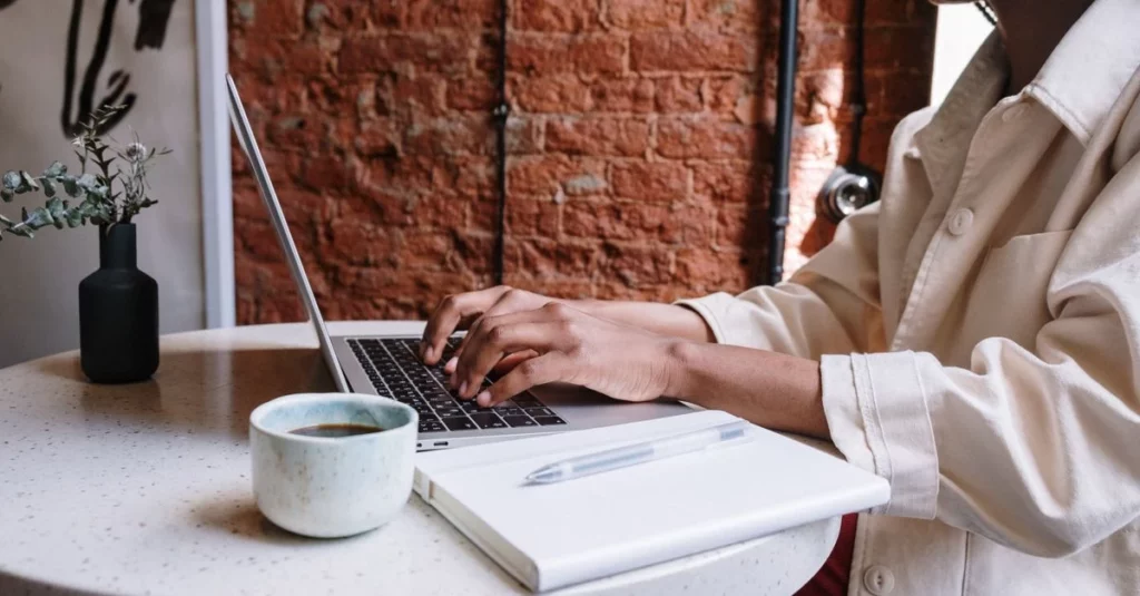 Person typing on laptop at desk with coffee cup and notebook, next to brick wall for comments widget website setup.