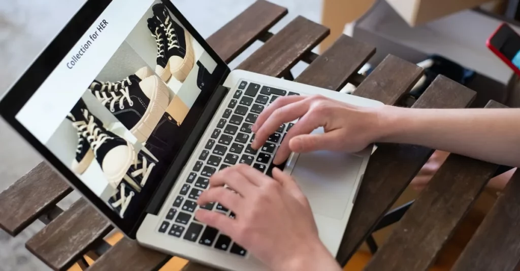 Hands typing on laptop displaying FAQ widgets website with shoe product images on wooden desk.